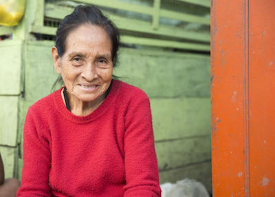 A woman smiles against a colorful wall at a market.